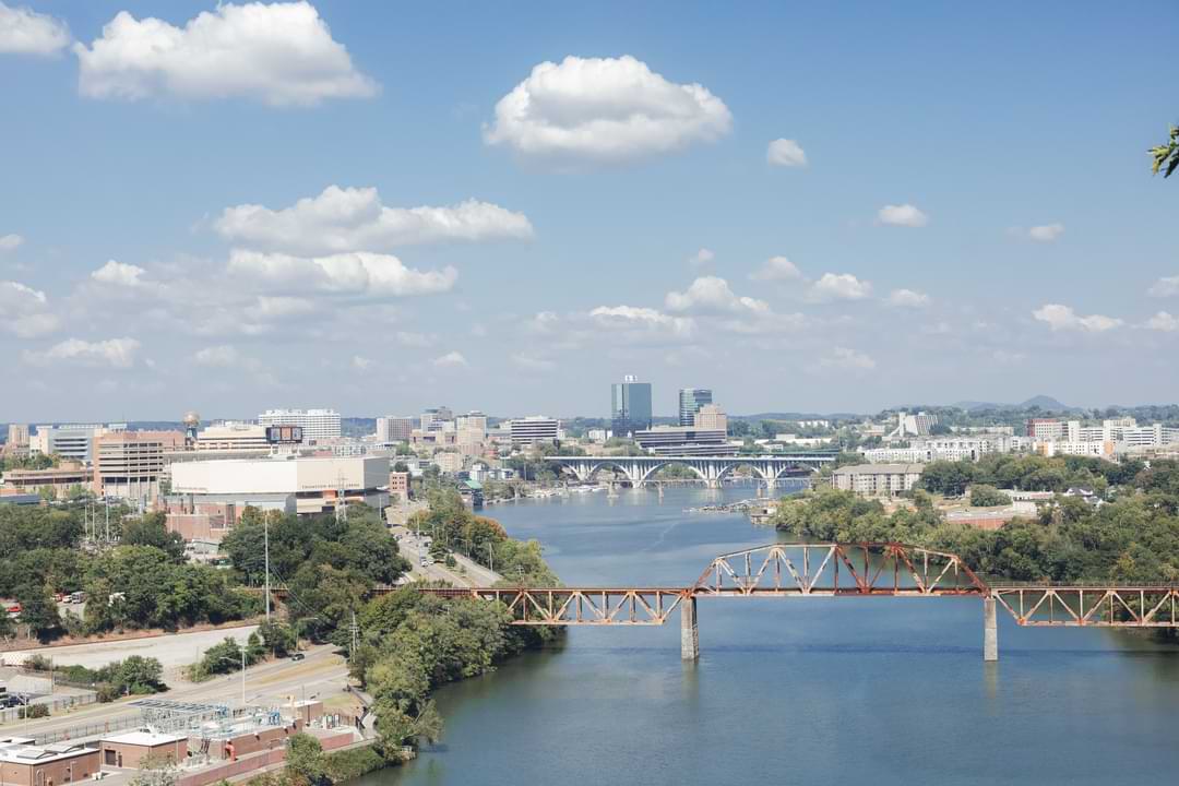 Panoramic view from a bridge, featuring a river flowing through the city with buildings lining the banks.