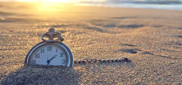 Pocket watch nestled in the sand of a beach at sunset